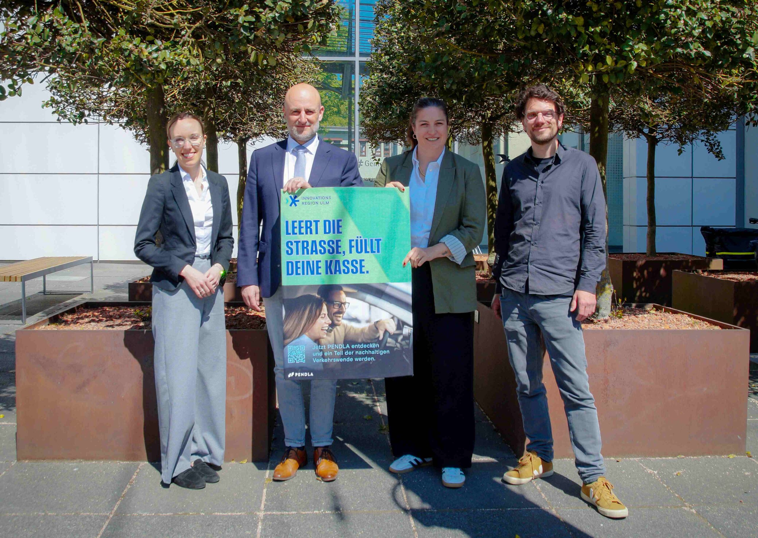 Pressefoto für Pendlerportal Pendla der Innovationsregion Ulm: 4 Personen, 2 halten das Kampagnenmotiv.
