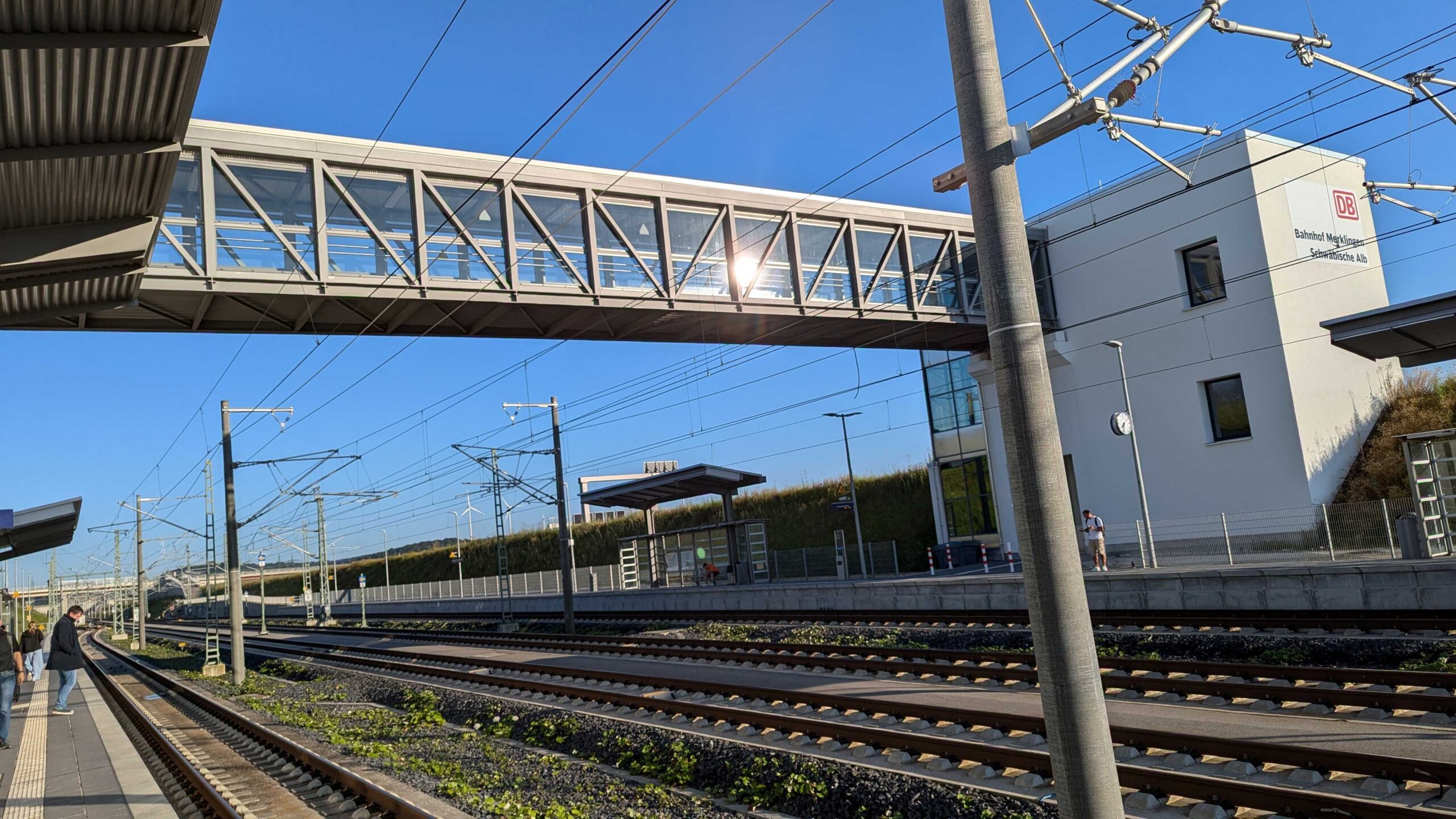 Der Bahnhof Merklingen-Schwäbische Alb. Schienen und eine Fußgängerbrücke, blauer Himmel, Sonnenschein.