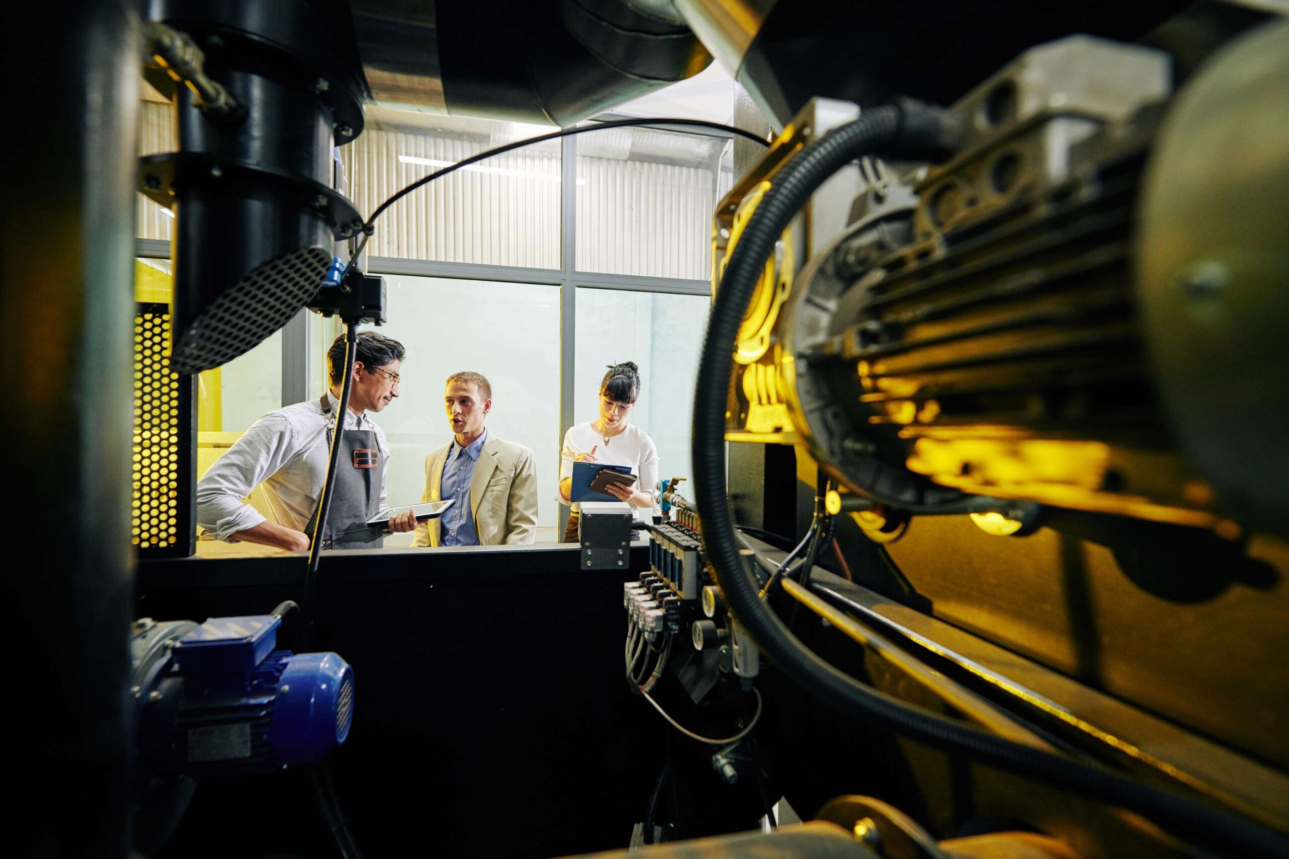 Personen stehen vor einer großen Industriemaschine und diskutieren.