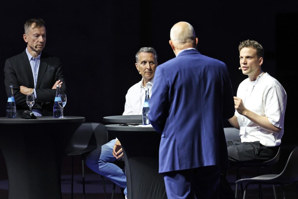 Vier Maenner in einer Podiumsdiskussion auf einer Buehne.