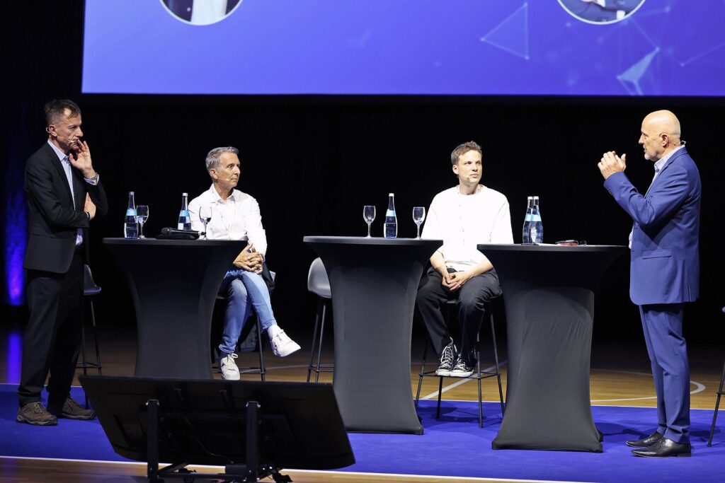 Diskussionspanel mit vier Personen auf einer Buehne waehrend einer Veranstaltung.