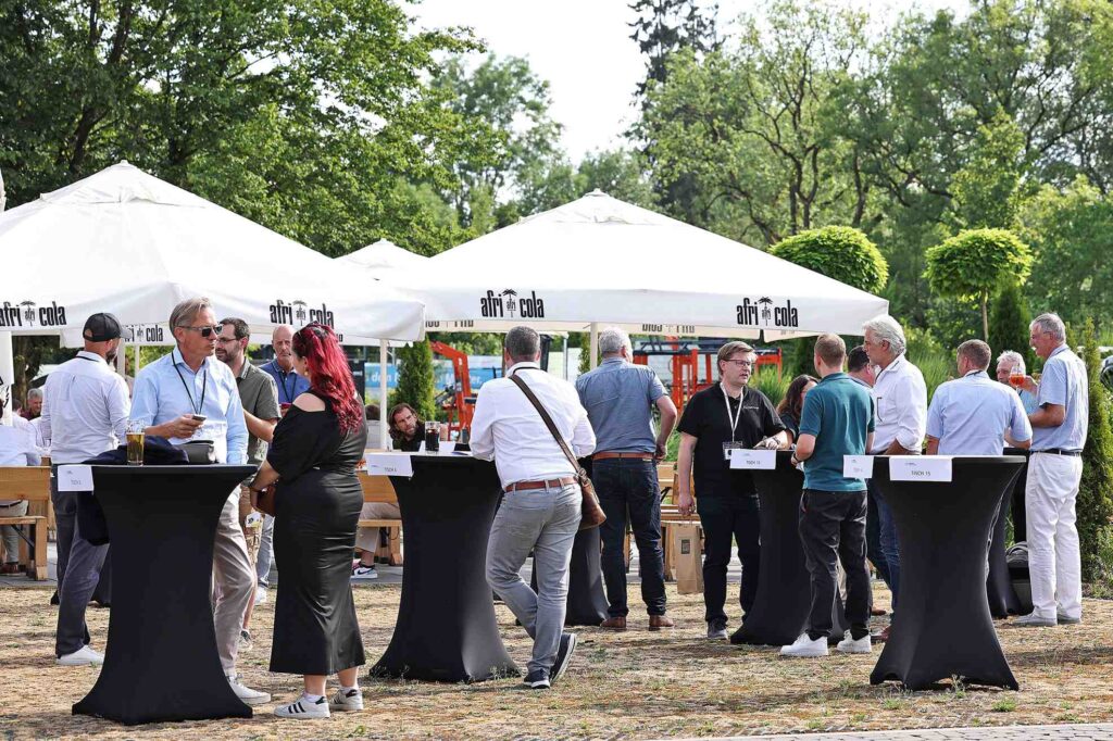Menschen stehen bei einer Outdoor-Veranstaltung unter weißen Zelten zusammen.