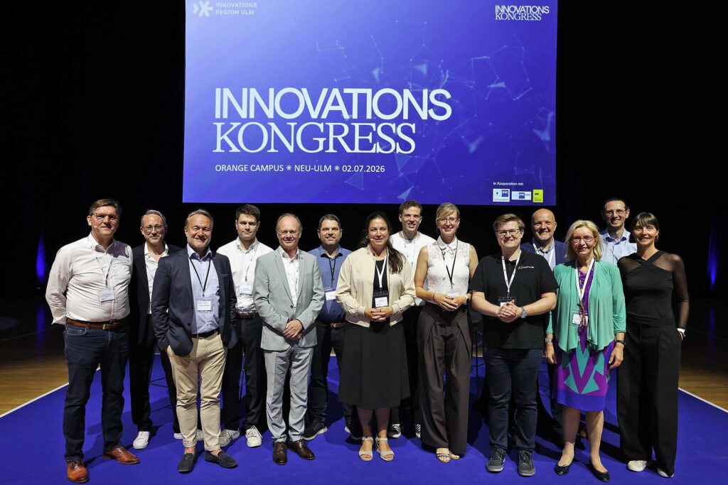 Eine Gruppe von Menschen posiert vor einer Leinwand mit der Aufschrift "Innovationskongress".
