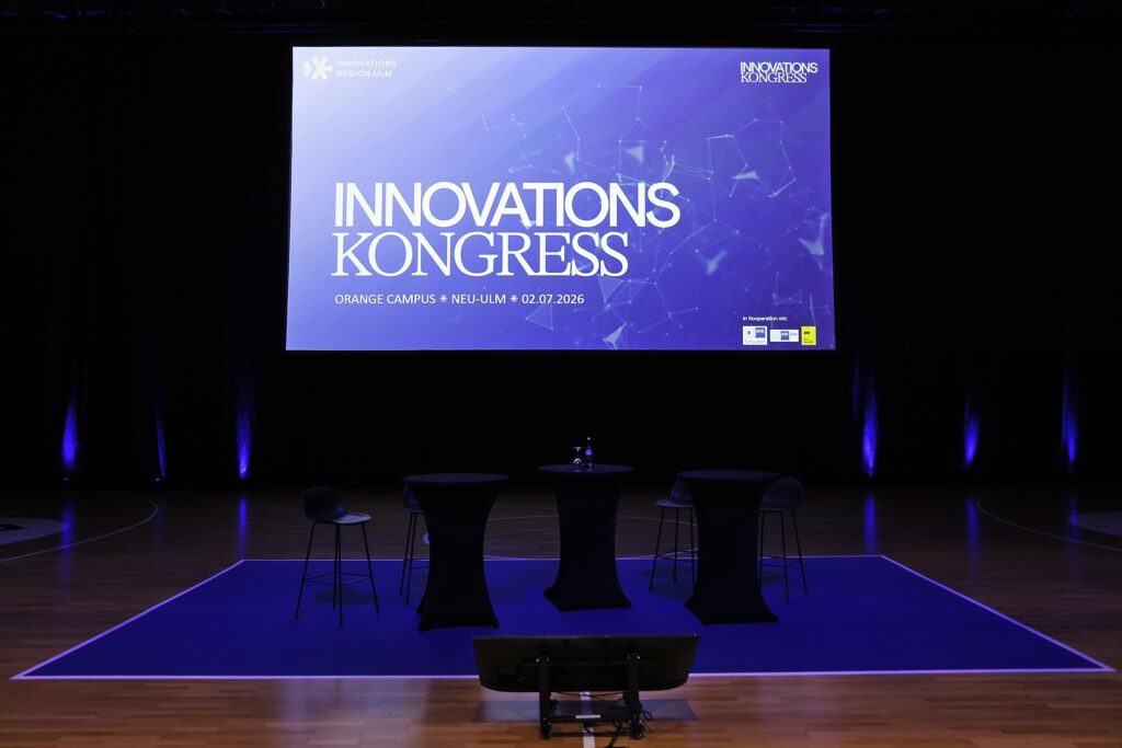Innovationskongress Buehne mit Praesentationsbildschirm und Pulten