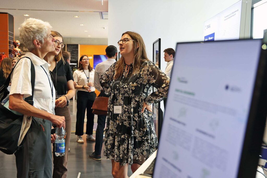 Teilnehmer unterhalten sich waehrend einer Messe an einem Ausstellungsstand.