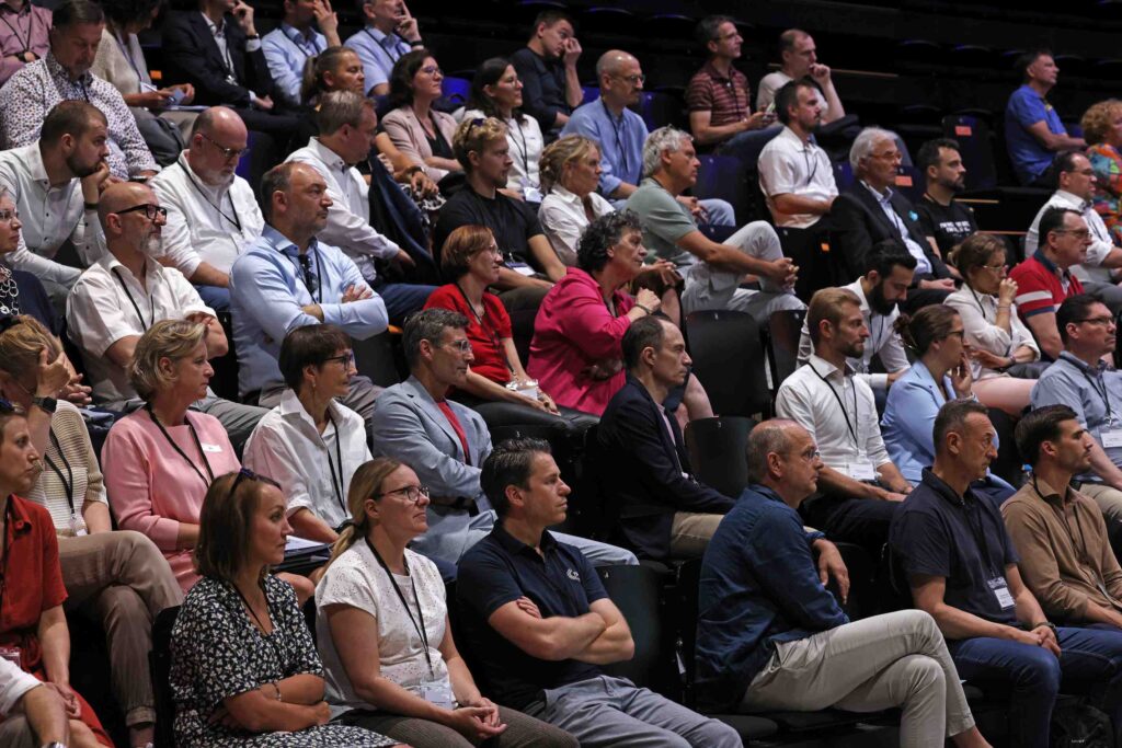 Eine große Gruppe von Menschen sitzt in einem Auditorium und folgt einem Vortrag.